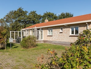 A single-story house with a brick exterior, a tiled roof, and a covered patio area. - Charming Bungalow on Ameland With a Beautiful Garden (Hollum)