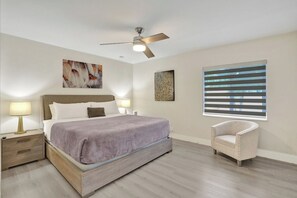 A bedroom with a bed, bedside lamps, a ceiling fan, artwork on the walls, and a window with blinds. - Chic 1BR Getaway Pool & Tiki Bar Blocks from Beach (Fort Lauderdale)