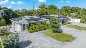 A modern house with solar panels, a paved driveway, and a well-maintained lawn. - Chic 1BR Getaway Pool & Tiki Bar Blocks from Beach (Fort Lauderdale)