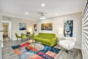 A modern living room with a green sofa, a white armchair, and colorful abstract art on the walls. - Tropical Beachside Bliss – Pool, Tiki Hut & Bar (Fort Lauderdale)