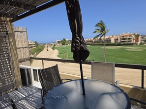 Ein Balkon mit Tisch und Stühlen, der auf einen Golfplatz und Gebäude blickt.
