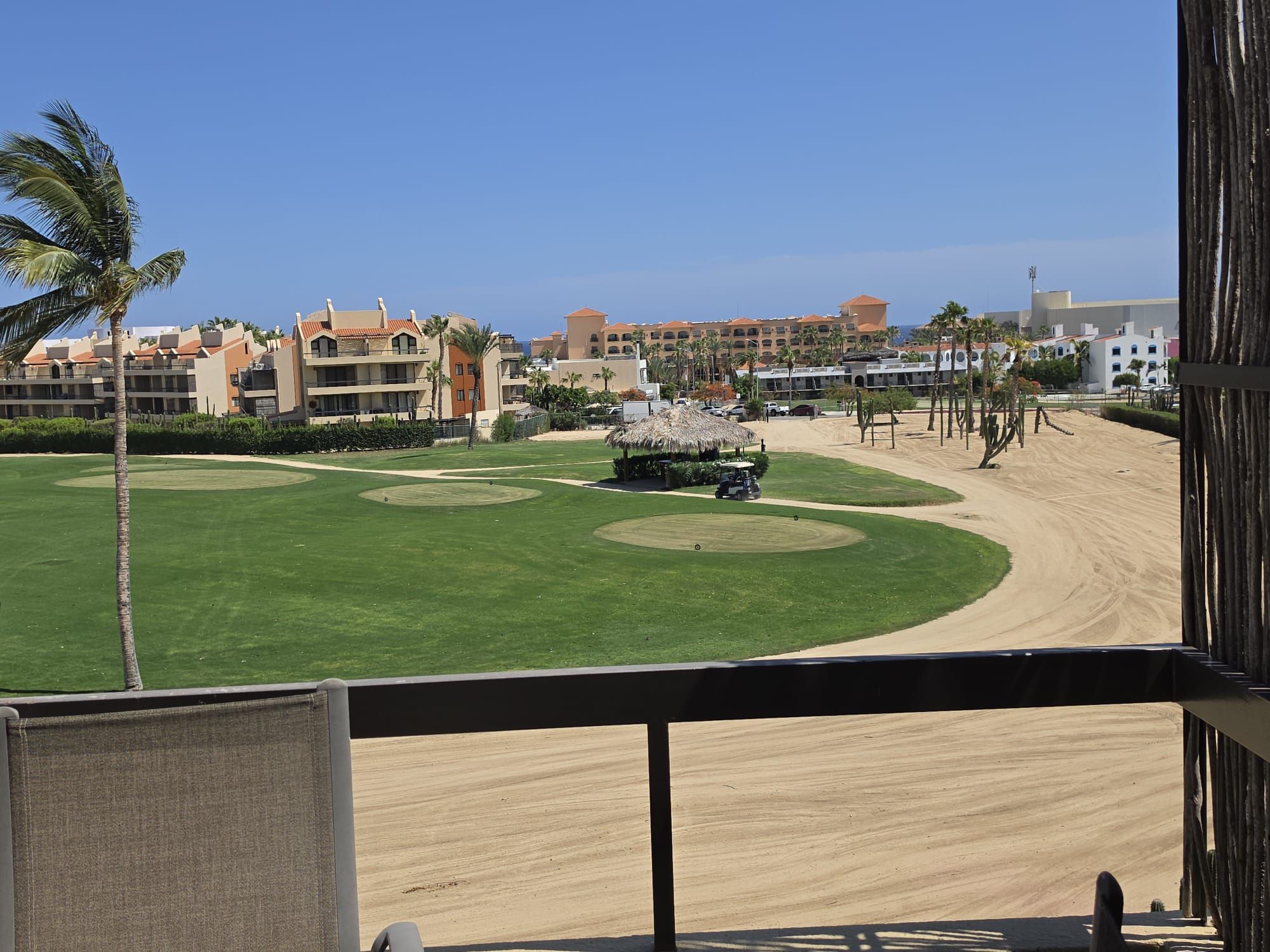 A golf course with a sand bunker, palm trees, and a building complex in the background.