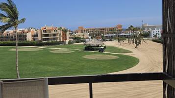 A golf course with a sand bunker, palm trees, and a building complex in the background.