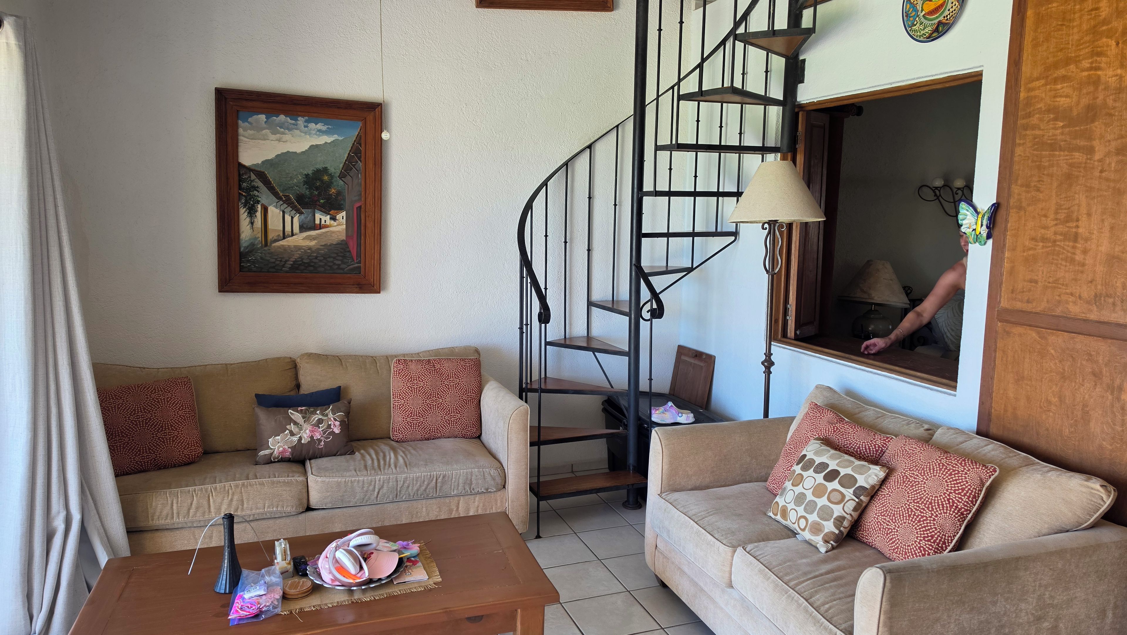 A living room with two sofas, a coffee table, a painting, a staircase, and a window with a view.