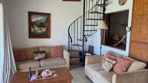 Sala de estar con dos sofás, una mesa de centro, un cuadro, una escalera y una ventana con vistas.