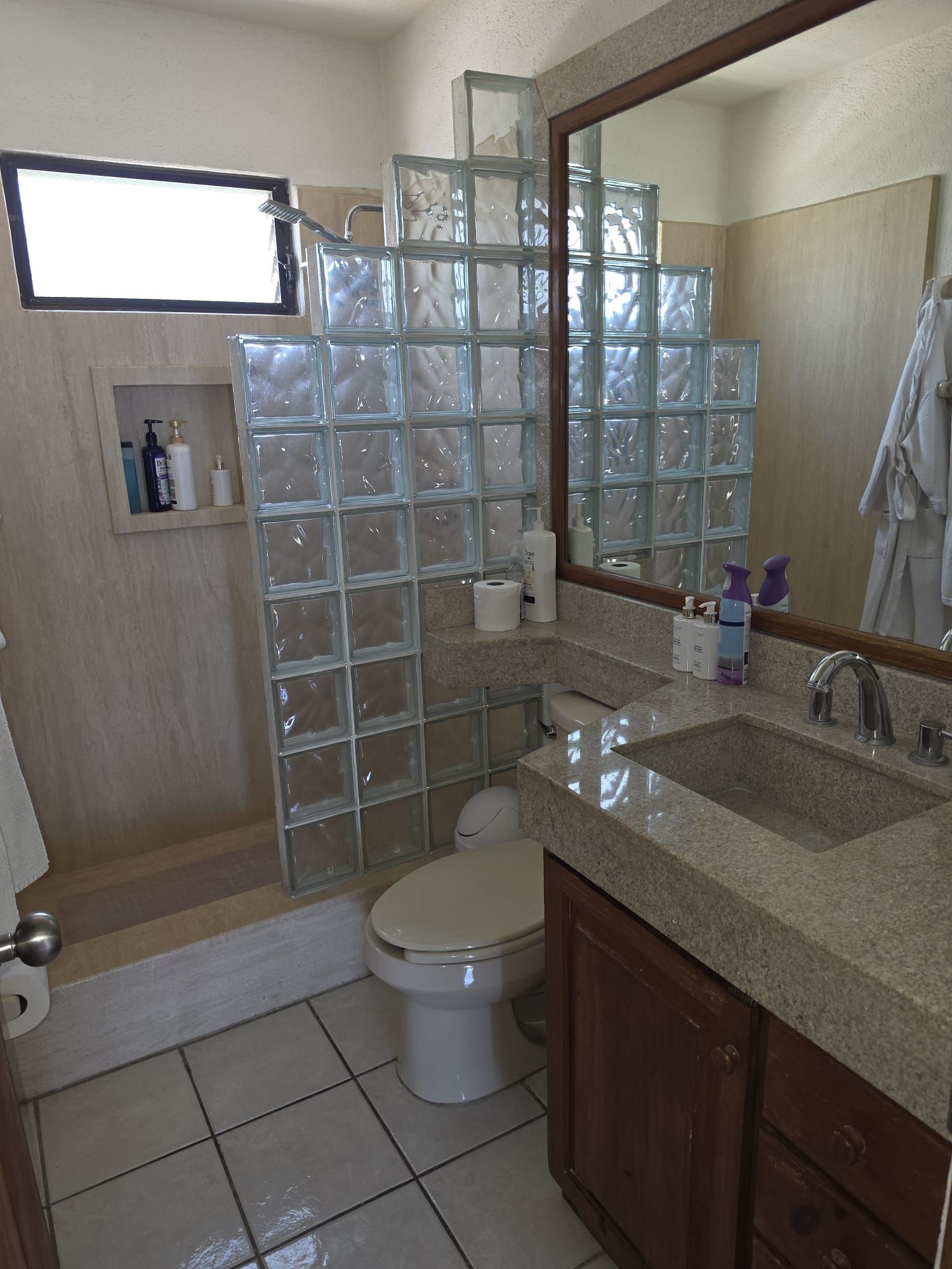 A bathroom with a glass shower enclosure, a toilet, a sink with a mirror, and toiletries on the countertop.