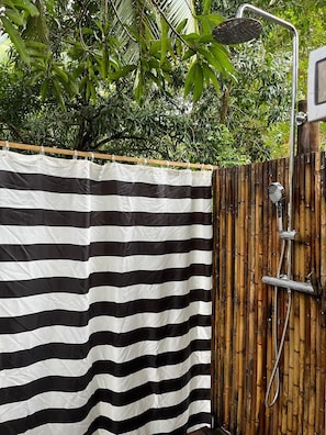 A shower area with a bamboo fence and a black and white striped shower curtain.