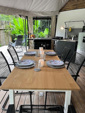 An outdoor dining area with a wooden table set for six, surrounded by black chairs.