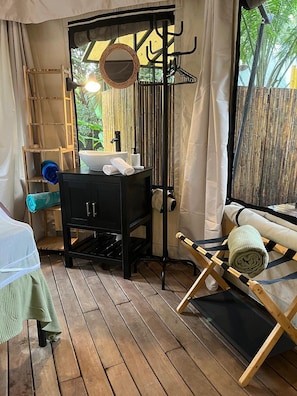 A compact room with a bed, a small table, a bench, and a window with a view of greenery.
