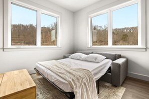 Un dormitorio con una cama, una mesita de noche y dos ventanas.