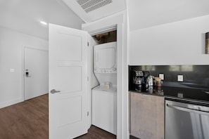 A modern kitchen with a built-in washer and dryer, stainless steel appliances, and a wooden floor. - Long Shadow Loft · 2BR Steps from MTB Trails (Bella Vista)