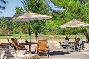 An outdoor seating area with tables and chairs, two striped umbrellas, and a decorative sculpture. - Long Shadow Loft · 2BR Steps from MTB Trails (Bella Vista)
