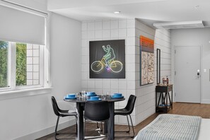 A modern room with a dining table set for two, a black chair, a bed with a striped cover, and a wall-mounted map. - Silent Hattie Loft · Studio by Tunnel Vision Trail (Bella Vista)