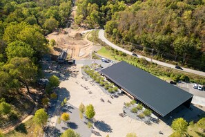 Une vue aérienne d’un parking avec un grand bâtiment, entouré d’arbres et bordé d’un chemin de terre.