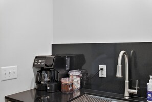 Una kitchenette con cafetera, dispensador de agua y jarra para café.