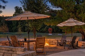 An outdoor patio with stone seating, two striped umbrellas, and a fire pit. - Play Thru Loft · 2BR w/ Balcony Near Back 40 (Bella Vista)