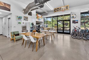 A cafe interior with tables, chairs, a coffee sign, artwork, and bicycles outside. - Play Thru Loft · 2BR w/ Balcony Near Back 40 (Bella Vista)