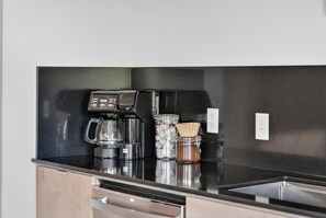 A kitchen counter with a coffee maker, a blender, and a jar of spices. - Play Thru Loft · 2BR w/ Balcony Near Back 40 (Bella Vista)