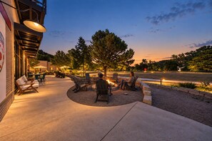 An outdoor seating area with chairs and tables, a fire pit, and a view of the street and trees. - Staggerwing Loft · 2BR Above Bike Shop & Café (Bella Vista)