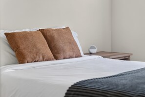 Un lit bien fait avec deux oreillers, une table de chevet avec une lampe et un réveil fixé au mur.