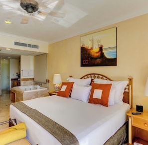 A hotel room with a large bed, a painting on the wall, a ceiling fan, and a bathroom with a bathtub. -  Ocean Front Spacious 2-bedroom condo in Cabo San Lucas with view of Lands End. (Cabo San Lucas)