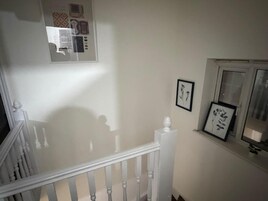 Una escalera con barandilla blanca, un cuadro colgado en la pared y una ventana con vistas.