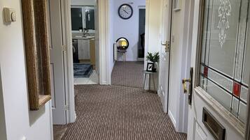 A hallway with carpeted flooring, a clock on the wall, and a door with a decorative glass panel.