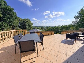 An outdoor patio with a table and chairs, surrounded by a wooden fence and overlooking a forested area. - La Colline Haute, private pool (SAGELAT)
