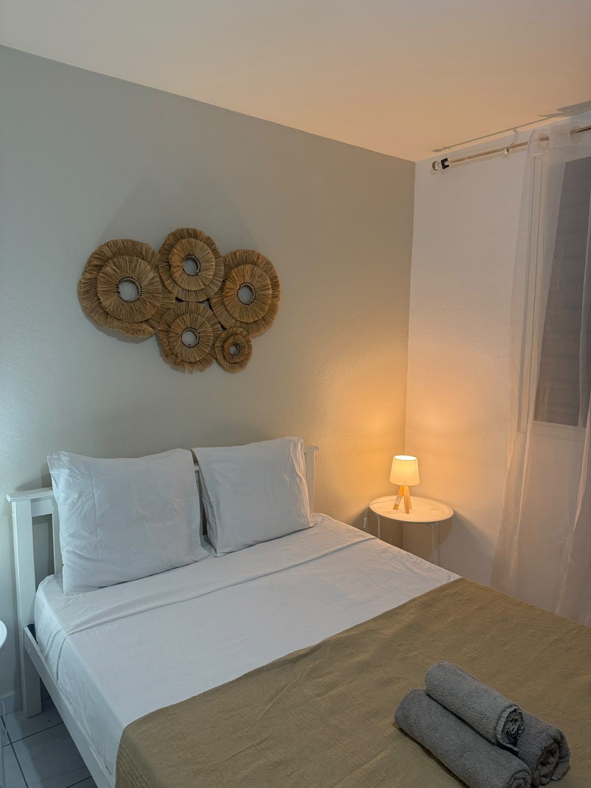 A hotel room with a bed, a nightstand with a lamp, a wall decoration, and a curtain.