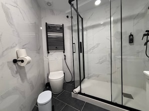 A modern bathroom with a glass-enclosed shower, a toilet, and a towel dispenser.