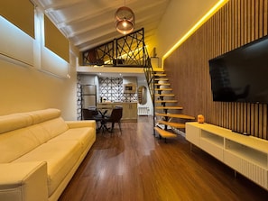 A modern living room with a sofa, dining table, chairs, a TV, and a staircase leading to an upper level.