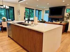A modern kitchen with a large island, built-in appliances, and a dining area with a sofa and table. - The Hidden Cedar | Private Lakefront Escape (Kent)