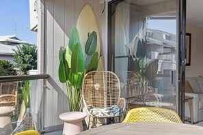 An outdoor seating area with wicker chairs and a table, a large plant, and a glass door leading to a balcony. - The Landing at Kailua Bay (Kailua-Kona)