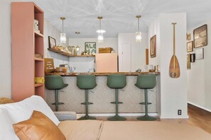 A modern kitchen with a bar area, green bar stools, pendant lighting, and a wooden paddle wall decoration. - The Landing at Kailua Bay (Kailua-Kona)