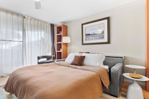 A hotel room with a large bed, a sofa, a chair, a small table, a bookshelf, and a framed picture on the wall. - The Landing at Kailua Bay (Kailua-Kona)