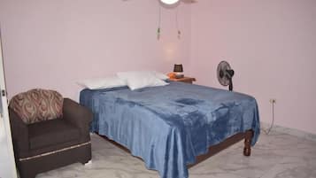 Un dormitorio con una cama, una silla, un ventilador de techo y un calentador de pared.