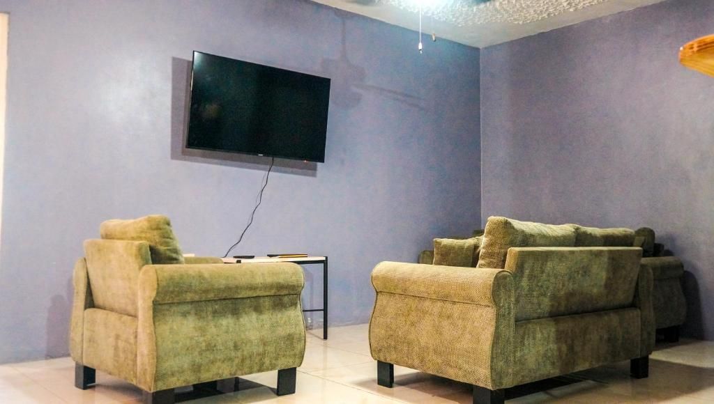 A living room with two green sofas, a flat-screen TV mounted on the wall, and a small table.