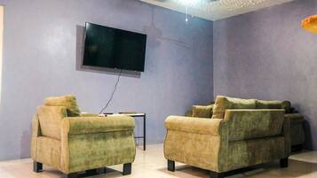 A living room with two green sofas, a flat-screen TV mounted on the wall, and a small table.