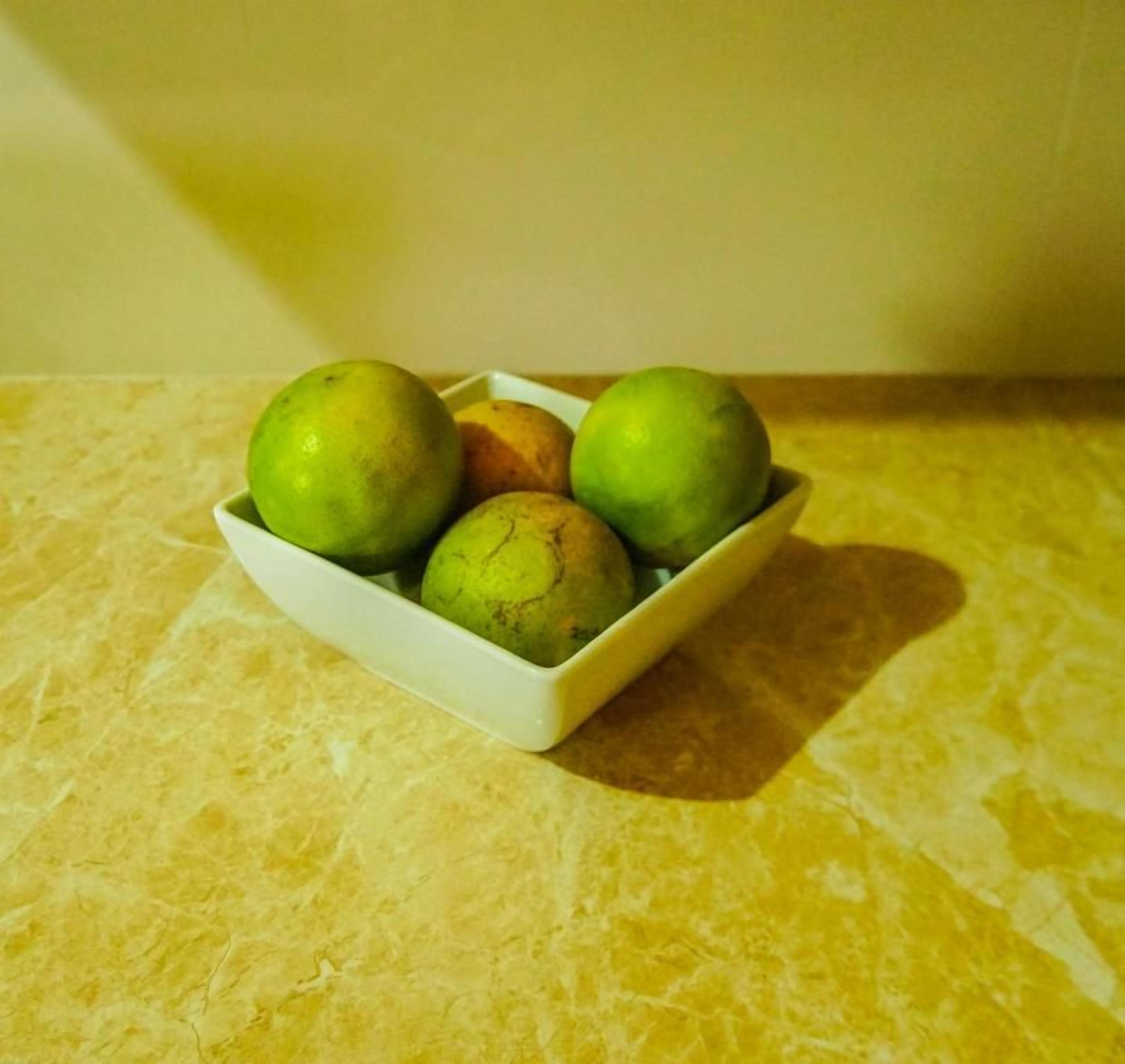 Un tazón blanco con varias frutas verdes sobre una superficie amarilla.