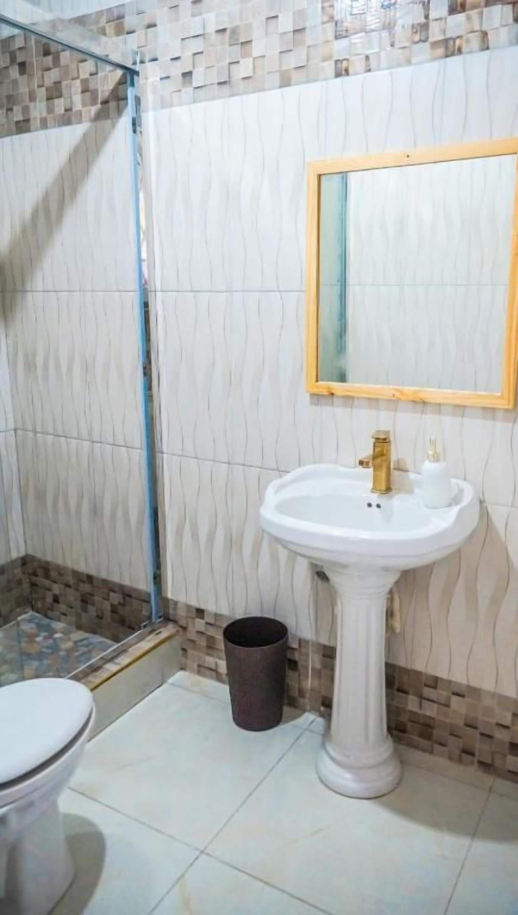 A bathroom with a pedestal sink, a mirror, and a shower area.