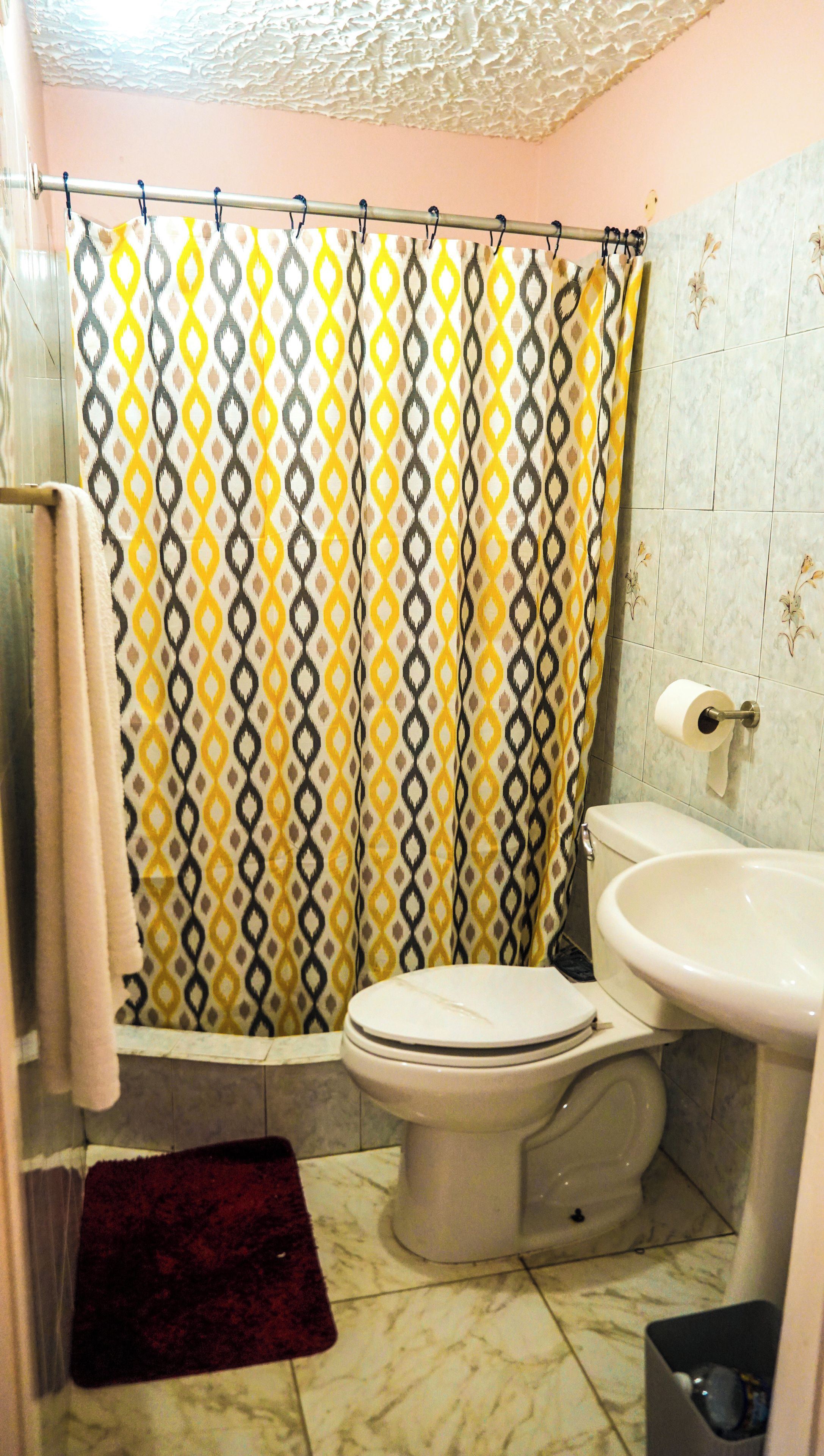 A bathroom with a patterned shower curtain, a toilet, a sink, and a trash bin.