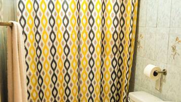 A bathroom with a patterned shower curtain, a toilet, a sink, and a trash bin.