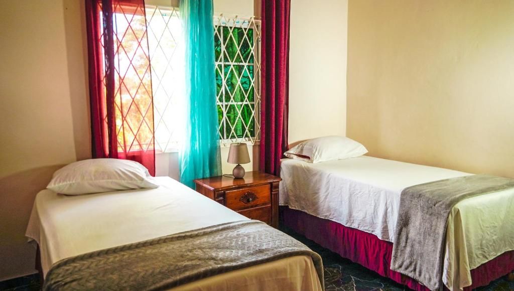 A room with two beds, a nightstand, and a window with curtains.