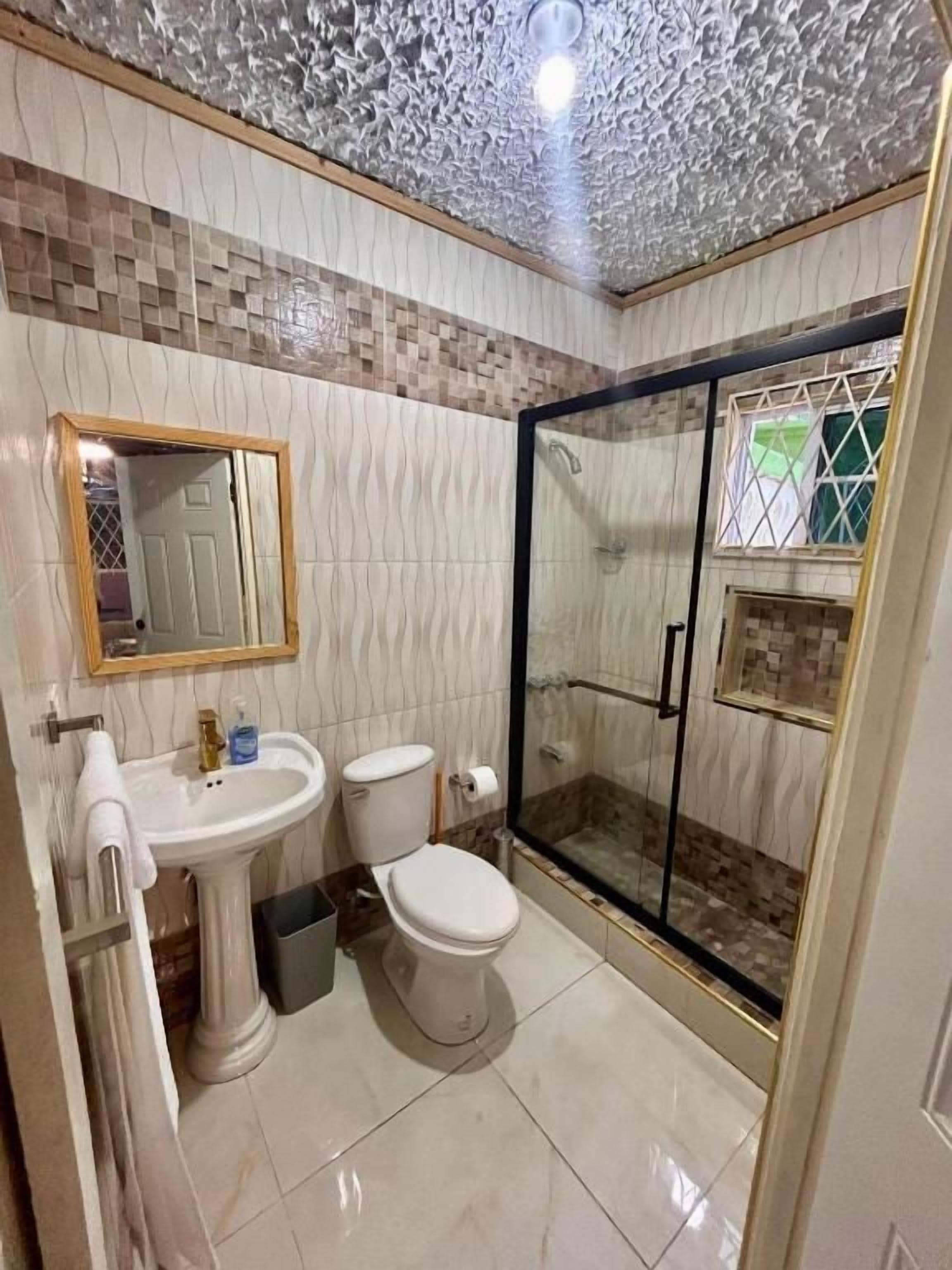 Un baño con lavamanos pedestal, inodoro y ducha con mampara de vidrio.