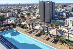 A rooftop pool with lounge chairs and umbrellas, surrounded by urban buildings.