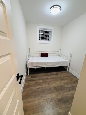 A room with a single bed, a window with blinds, a door with a handle, and a wooden floor.
