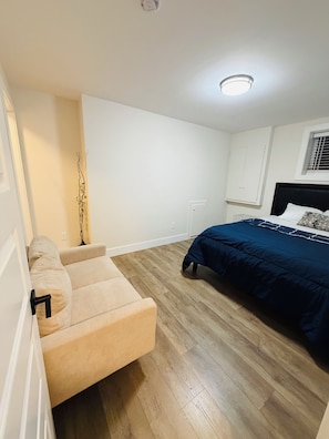 A bedroom with a bed, a sofa, and a wooden floor.