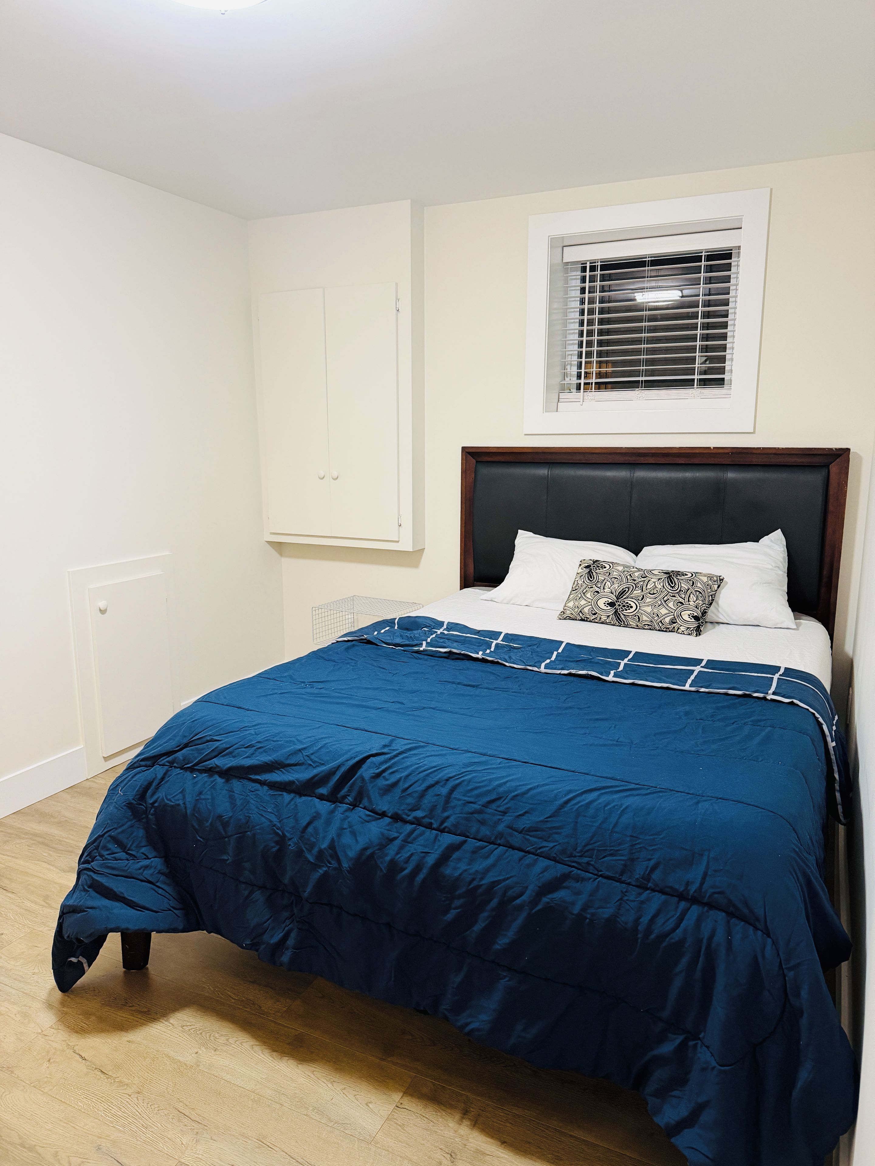 A bedroom with a bed, a window with blinds, a wardrobe, and a radiator.