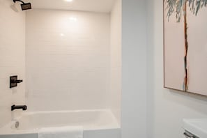 Et badeværelse med et hvidt badekar, brusearmatur på væggen og et billede.