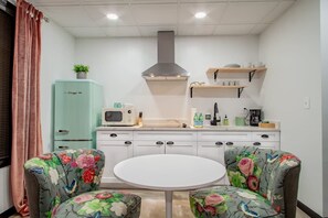 A compact kitchen with a microwave, toaster, and a hanging range hood. There are two chairs with floral upholstery and a small round table. - Vintage Studio - Walk to the White House (Washington)